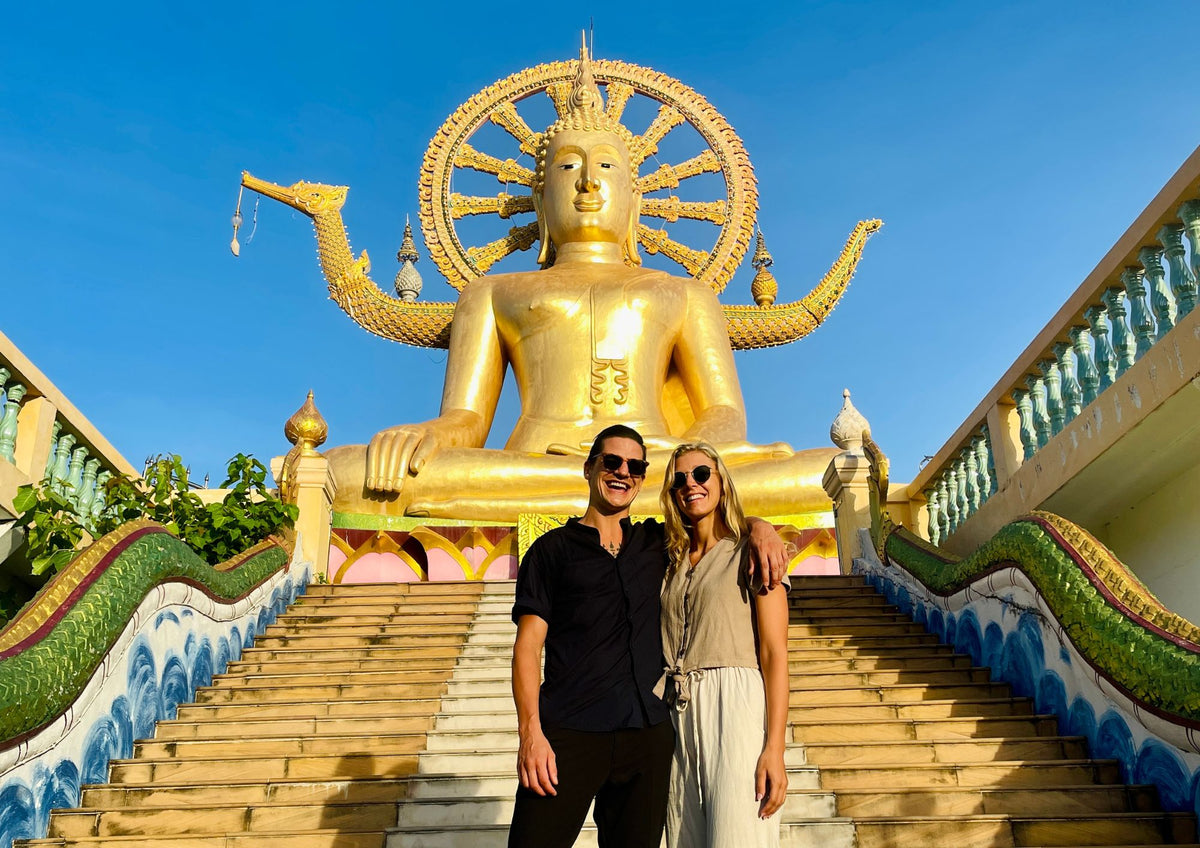 Couple standing on the naga staircase below the gold Big Buddha statue at Wat Phra Yai, Koh Samui