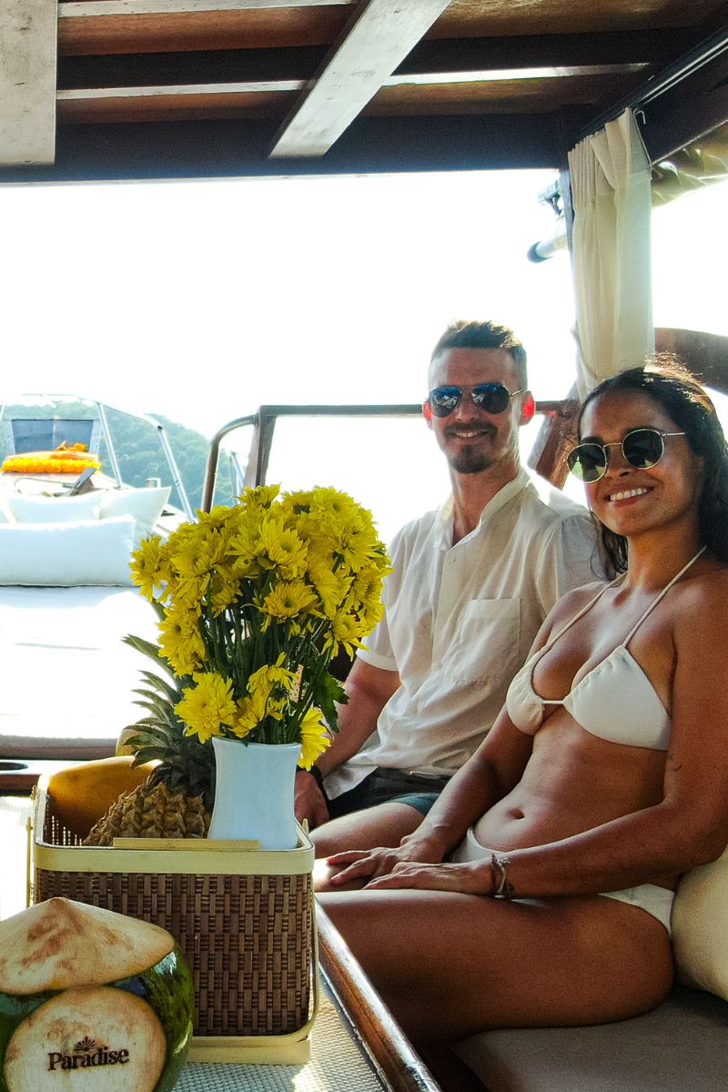 Man and woman sitting on a boat with yellow flowers and a pineapple.