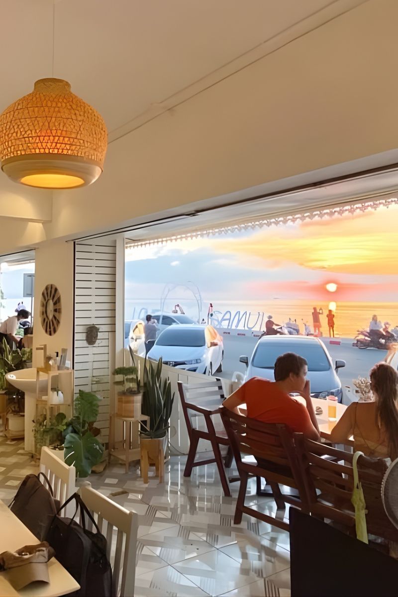 Dining area with people sitting at tables, large window showing outdoor scene.