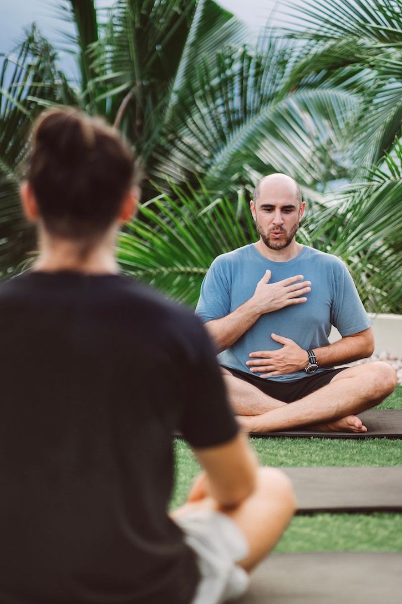 Two people practicing yoga outdoors with greenery in the background