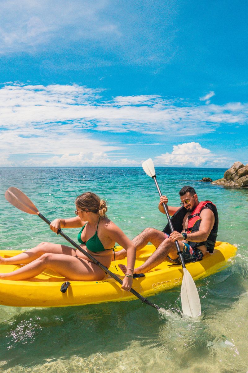 Two people kayaking in clear blue water with a rocky island in the background.