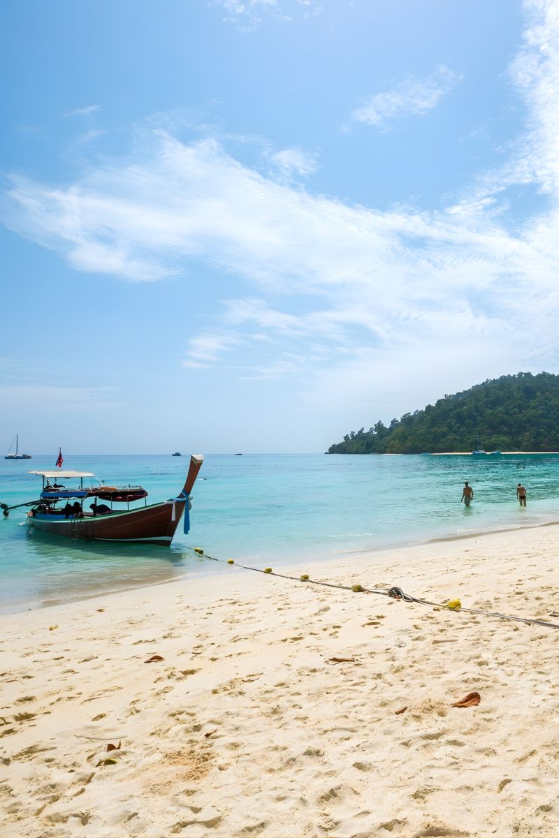 Beach scene with a boat in clear blue water and a tropical island in the background.