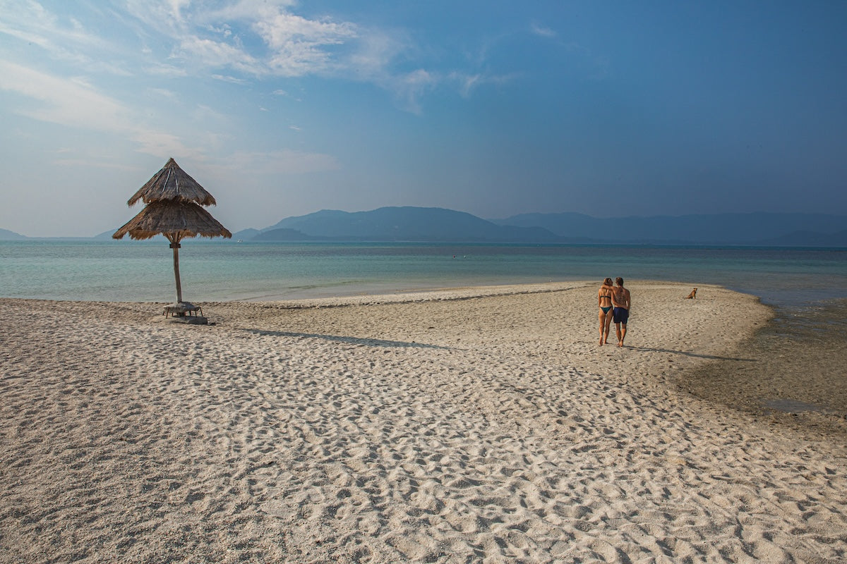 Happy couple walking along the beach in Koh Mad Sum (Pig Island) on their luxury longtail experience 