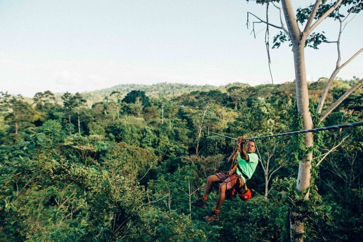 A rider on a zipline crossing high above dense green jungle canopy in Koh Samui