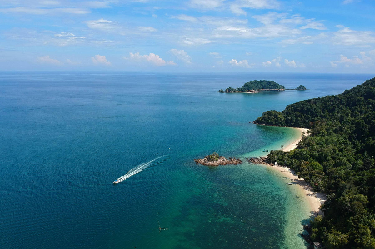 Aerial view of a private speedboat crossing clear turquoise water past a white sand beach and small tropical islands
