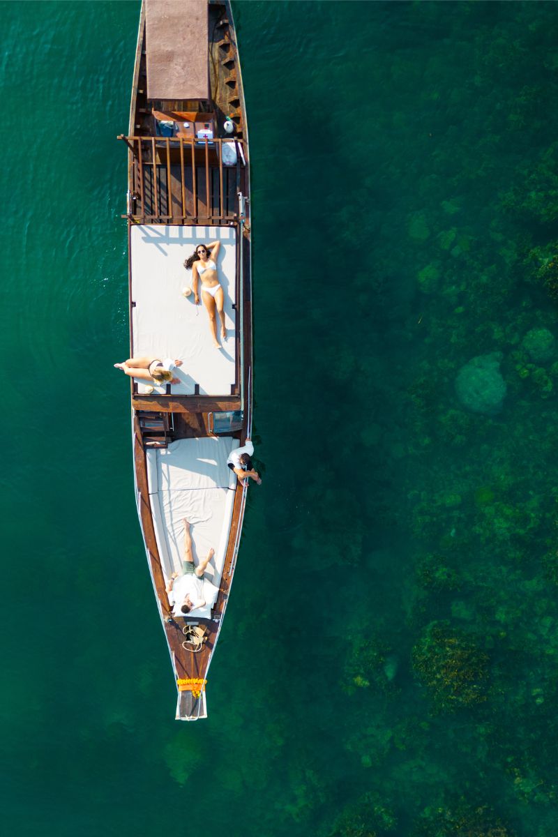 Aerial view of a long wooden boat with people on a clear blue water background