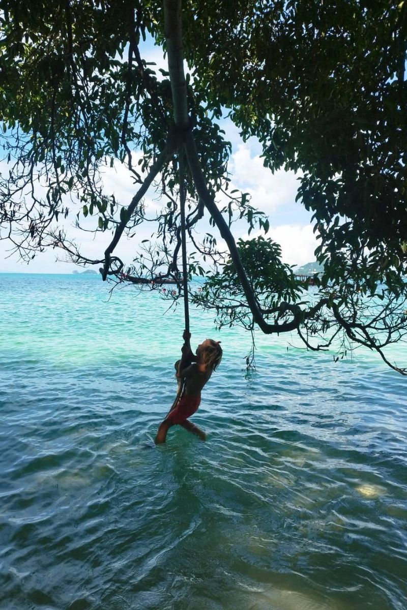 Person on a swing hanging above a body of water with trees and sky in the background