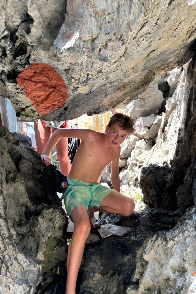 Person climbing a rocky cliff with another person in the background
