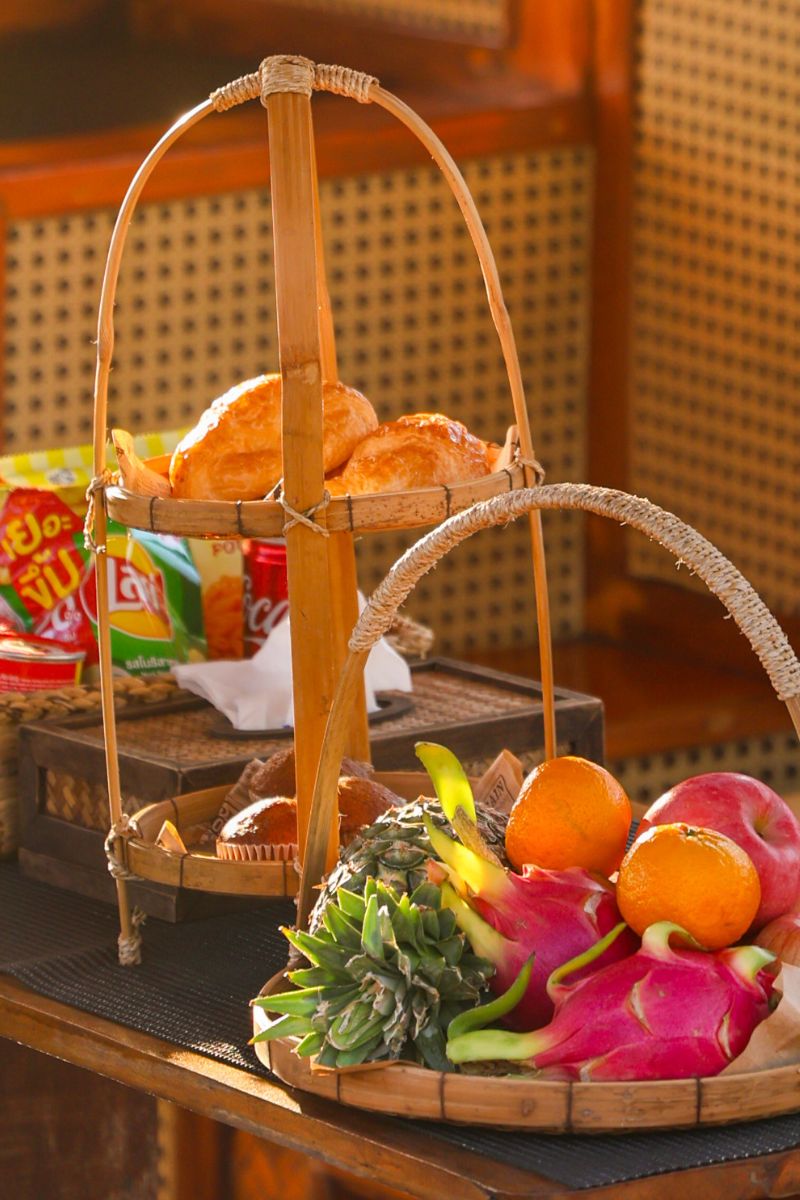 Bamboo fruit basket with fruits and snacks on a wooden table.