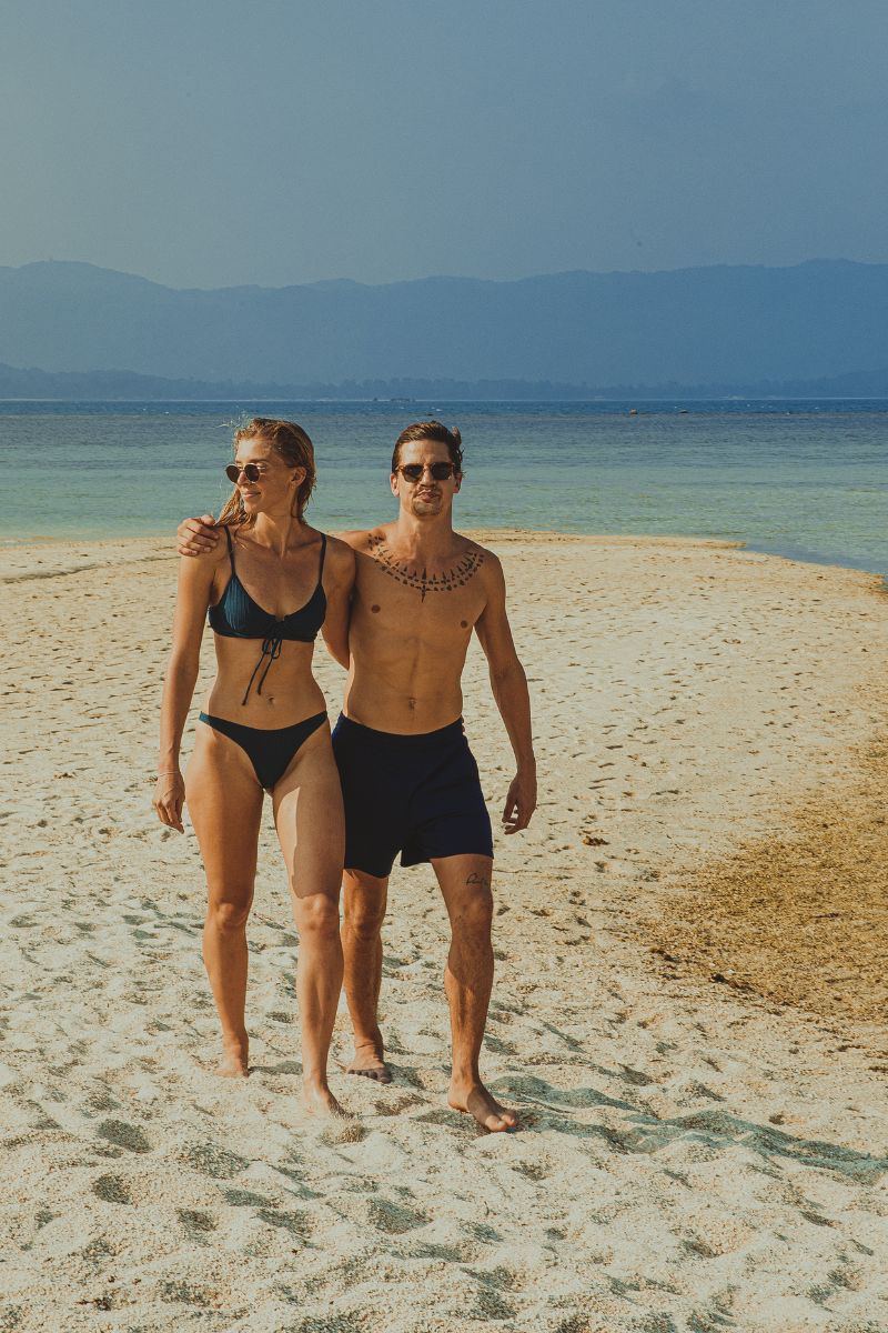 Two people walking on a sandy beach with mountains in the background