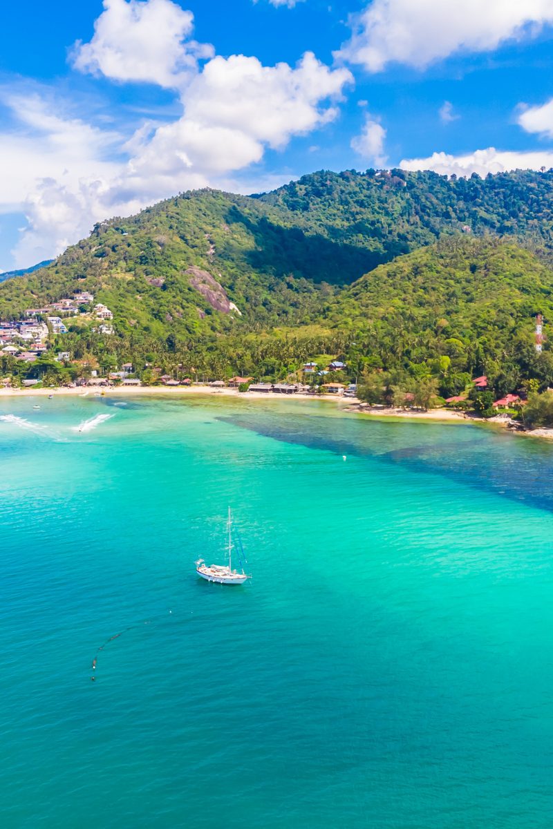 Aerial view of a sailboat anchored in a turquoise bay off Koh Samui