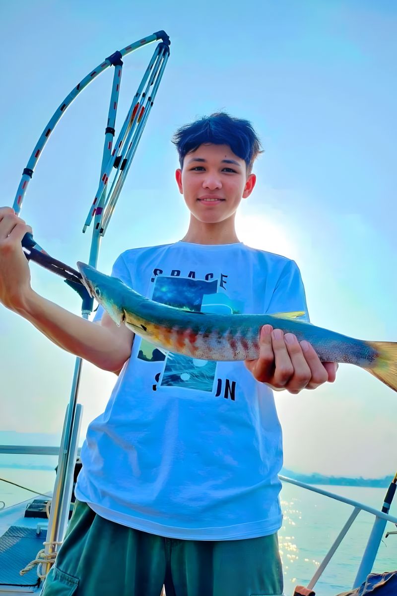 Person holding a colorful fish on a boat with a clear sky background