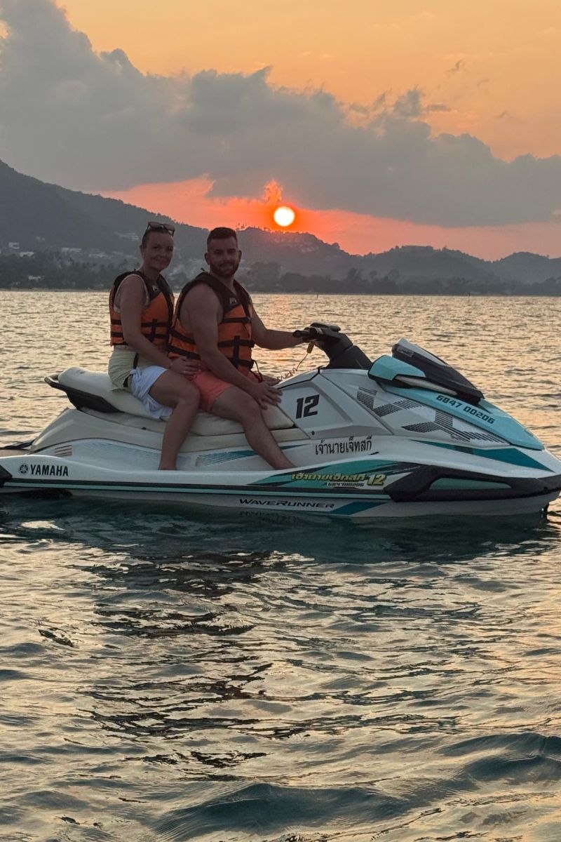 Two people on a jet ski in the water with a sunset in the background