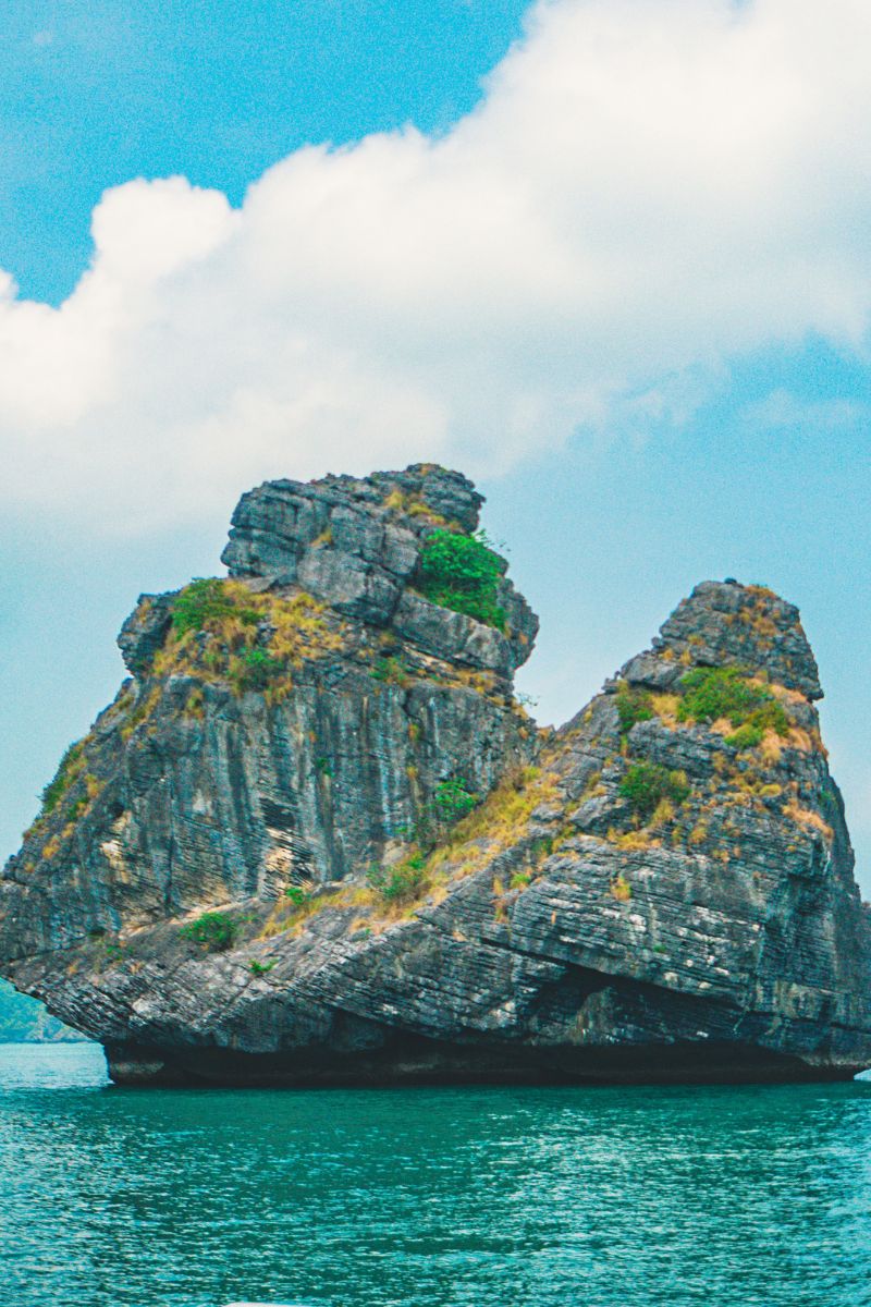 Rock formation in the middle of a body of water with a blue sky and clouds.