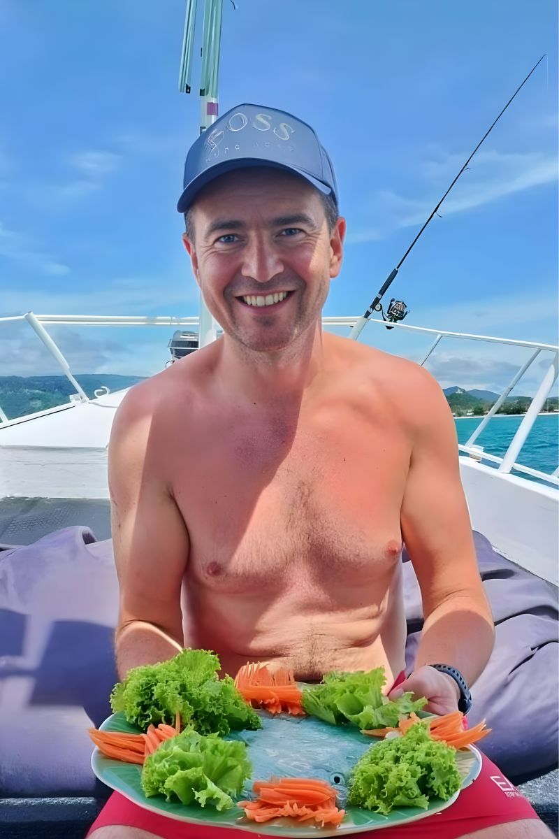 Man on a boat holding a plate of food with a scenic background