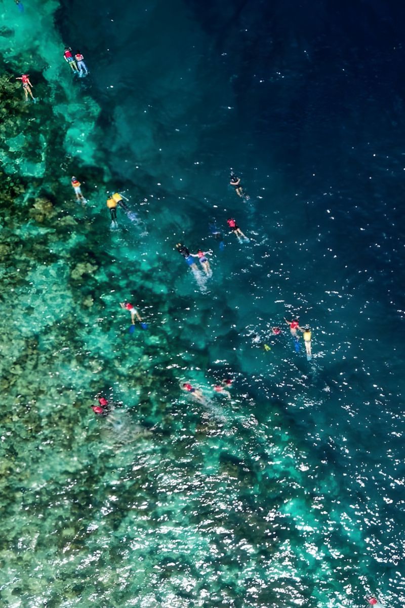Aerial view of people snorkeling in a clear blue underwater cave.