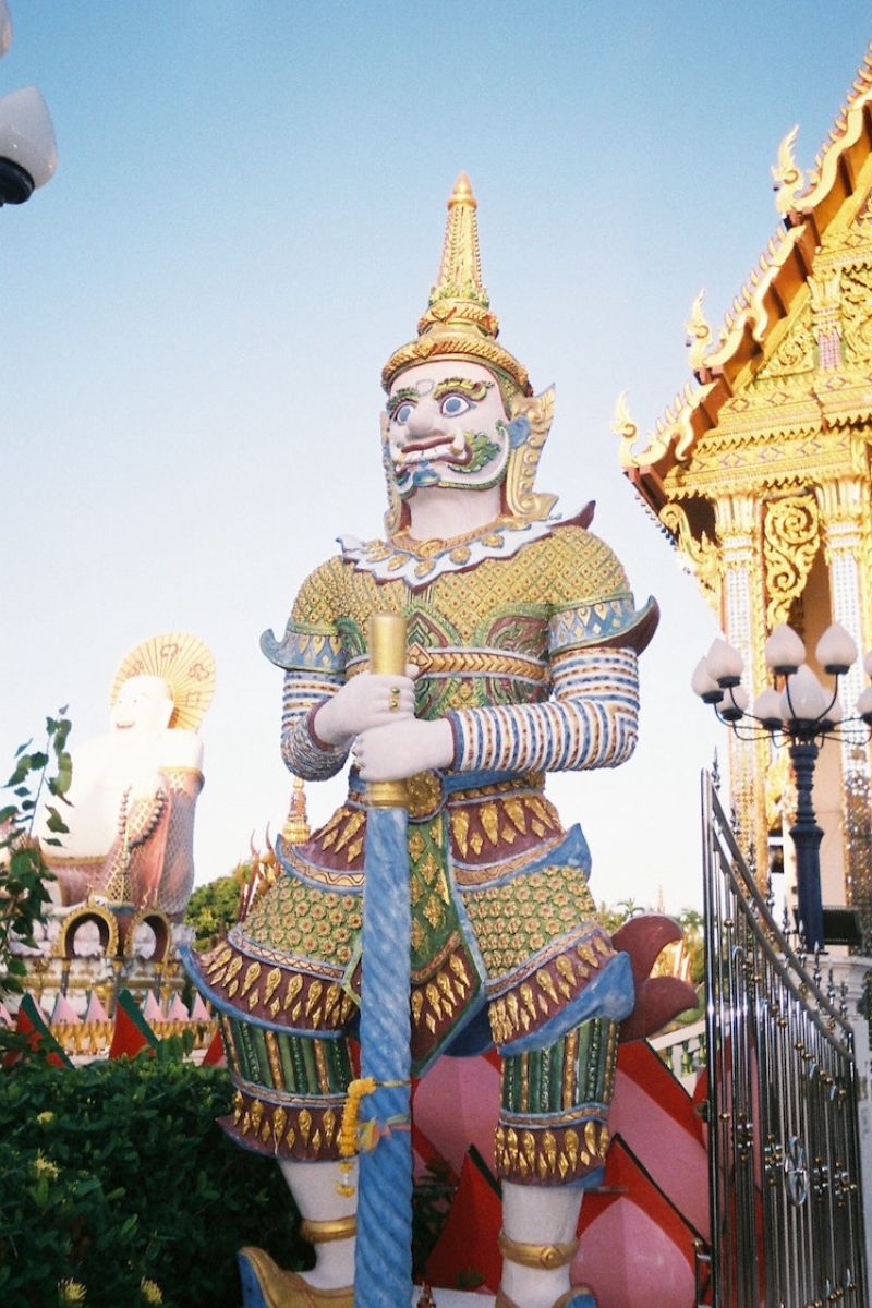 Colorful statue of a guardian figure with intricate details against a clear blue sky.