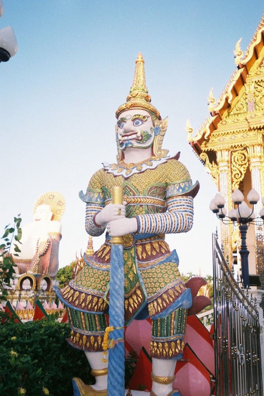 Colorful statue of a guardian figure with intricate details against a clear blue sky.