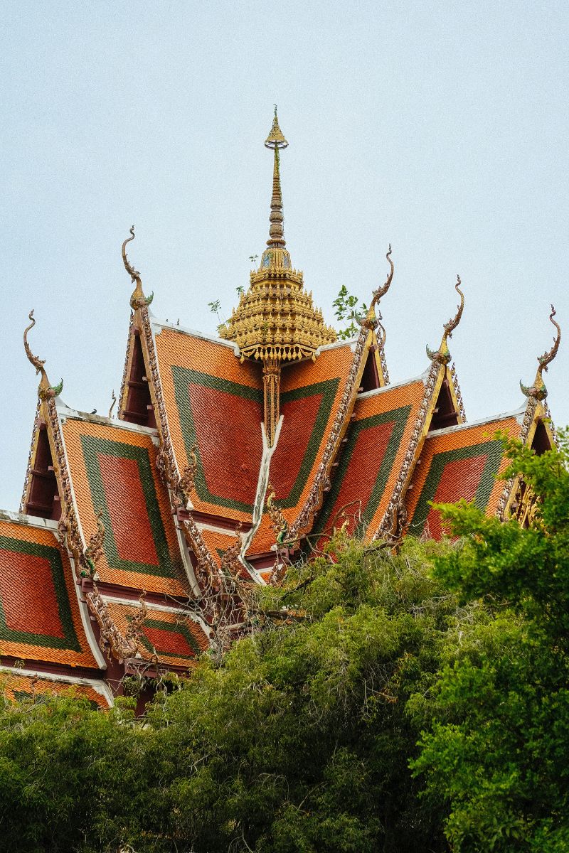 Traditional Thai temple with ornate roof design surrounded by green trees