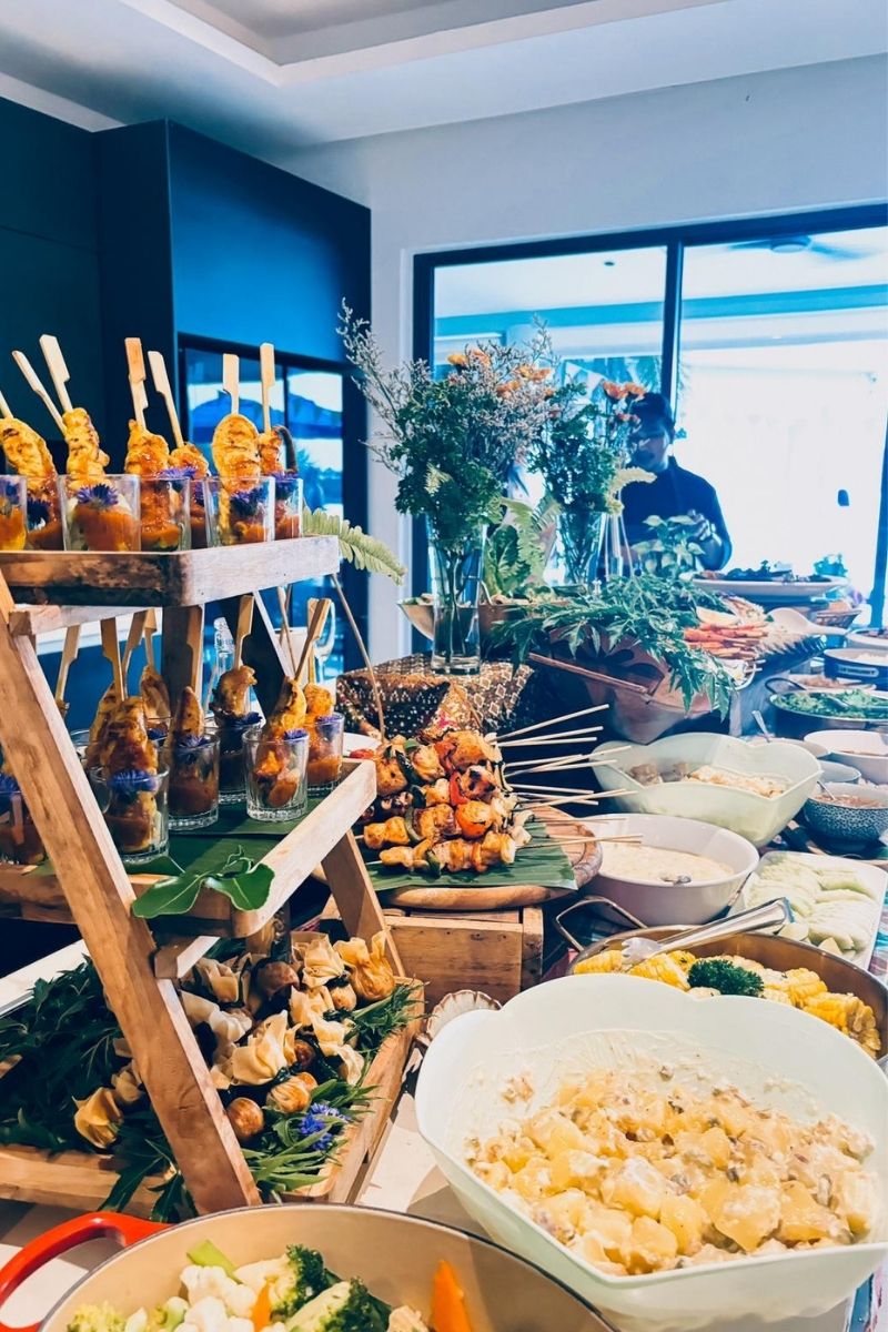 Buffet table with various dishes including skewered food and salads in a bright room.