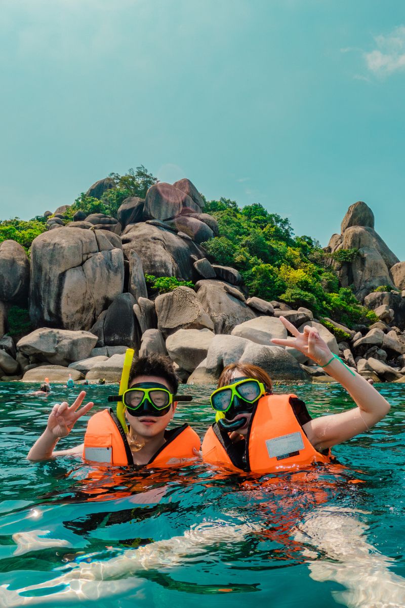 Two people in snorkeling gear in clear blue water with rocky landscape in the background