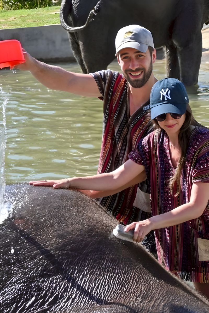 Two people interacting with elephants in a water body