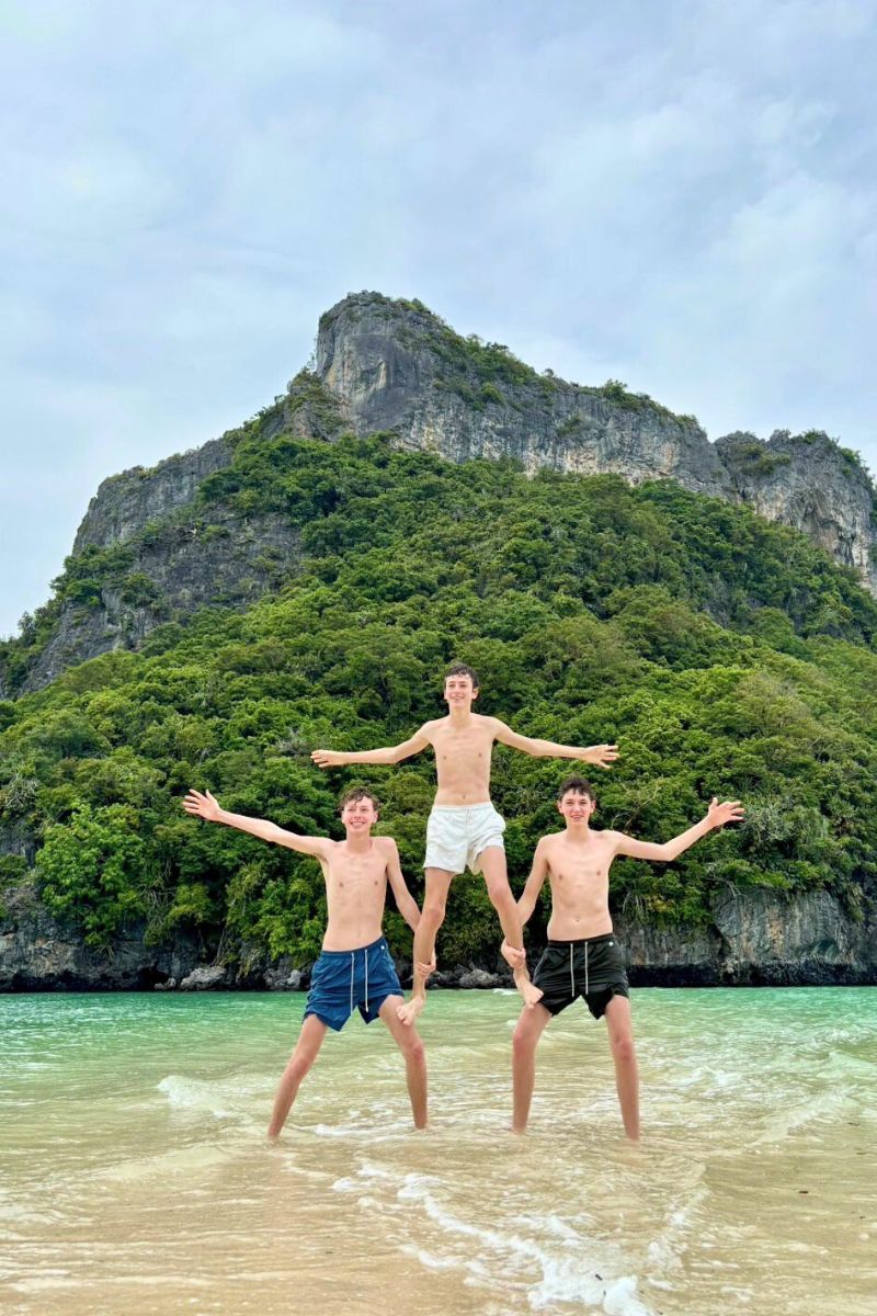 Three people posing on a beach with a rocky island in the background
