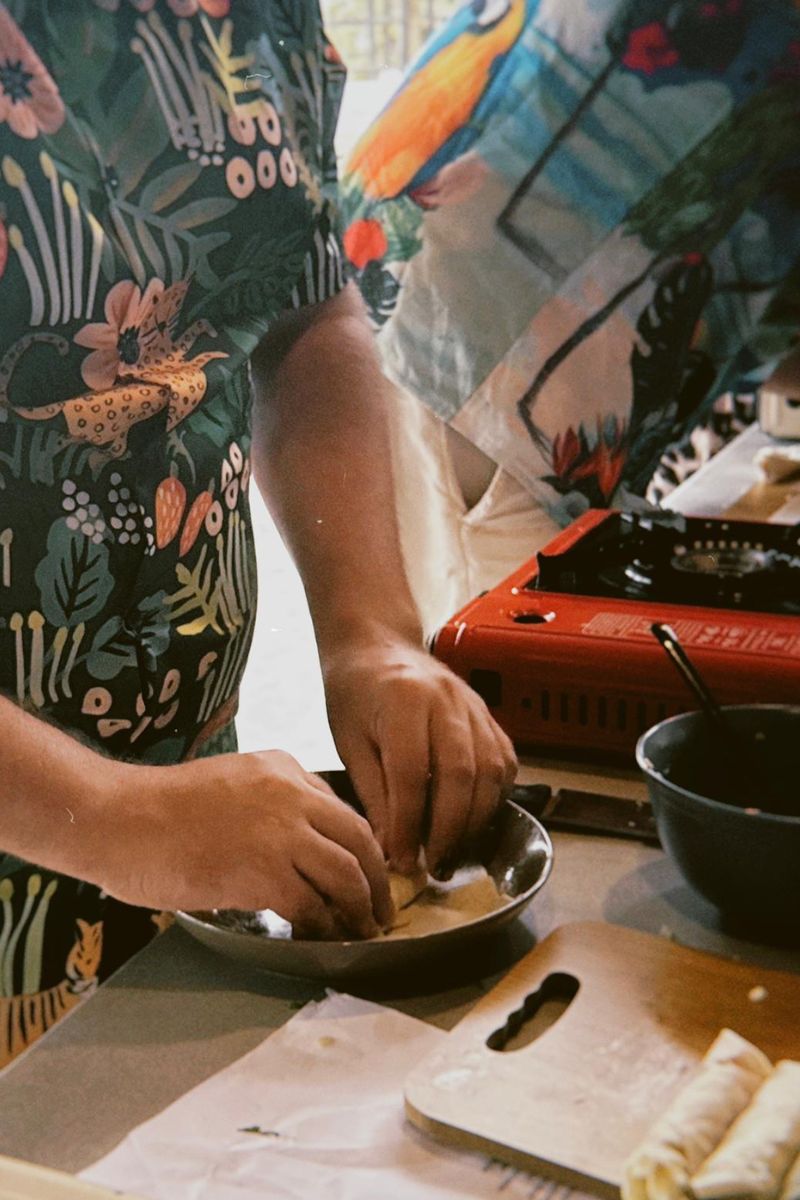 Person preparing food on a stove with a floral-patterned shirt
