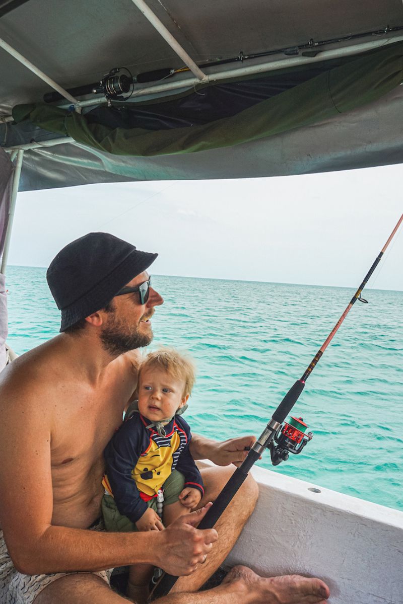 Man and child on a boat fishing with turquoise water in the background