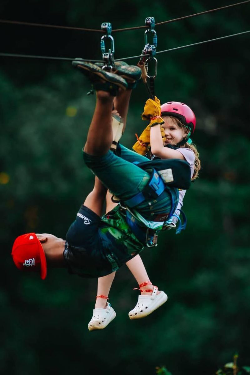 Person and child on a zip line with green forest background