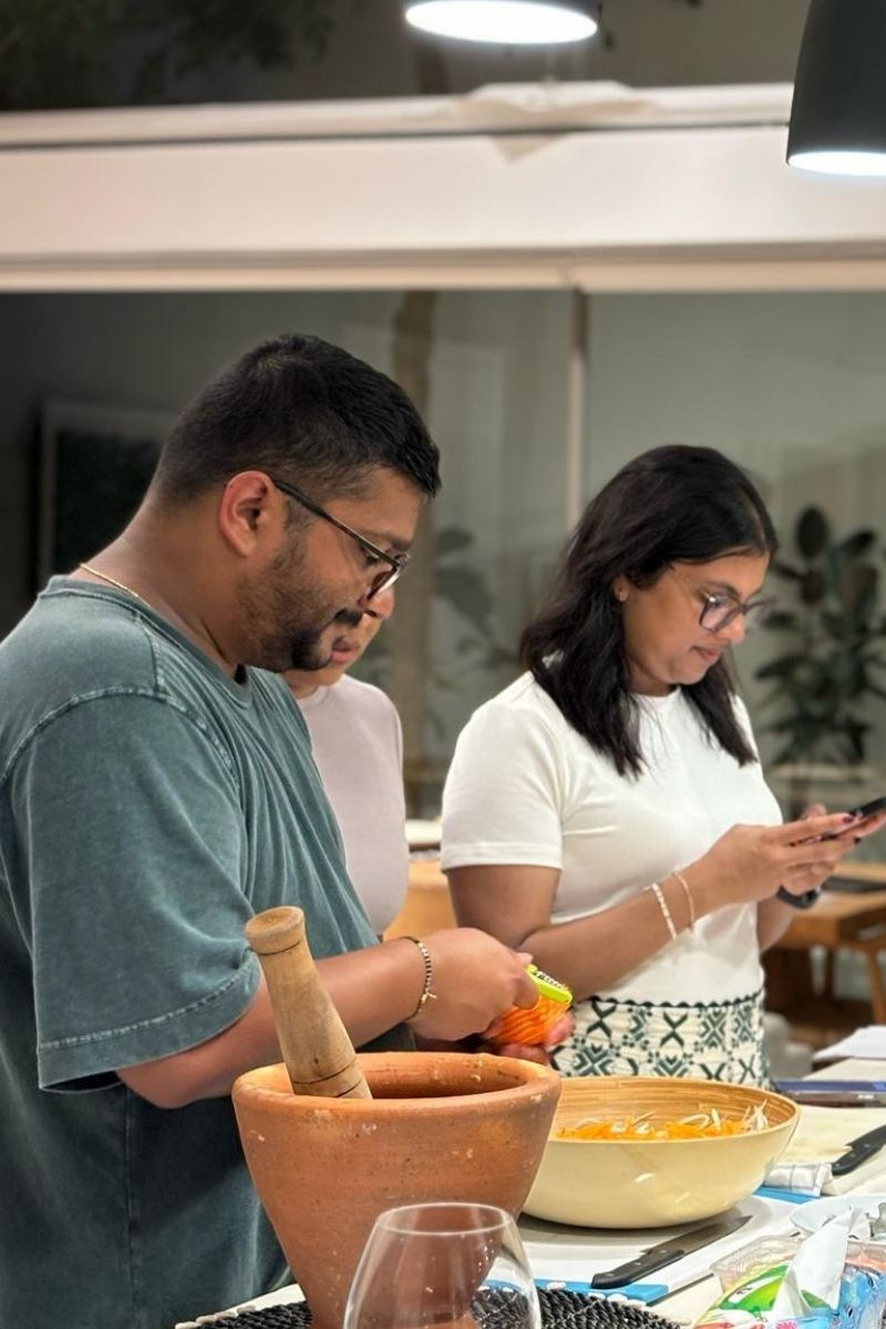 Two people in a kitchen setting, one using a smartphone and the other working with ingredients.