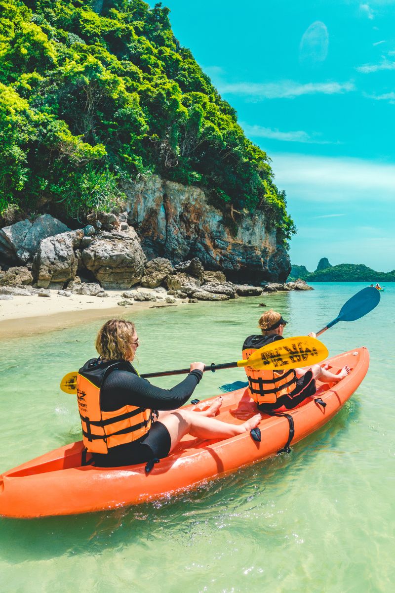 Two people kayaking in clear water with a scenic background of cliffs and sky.