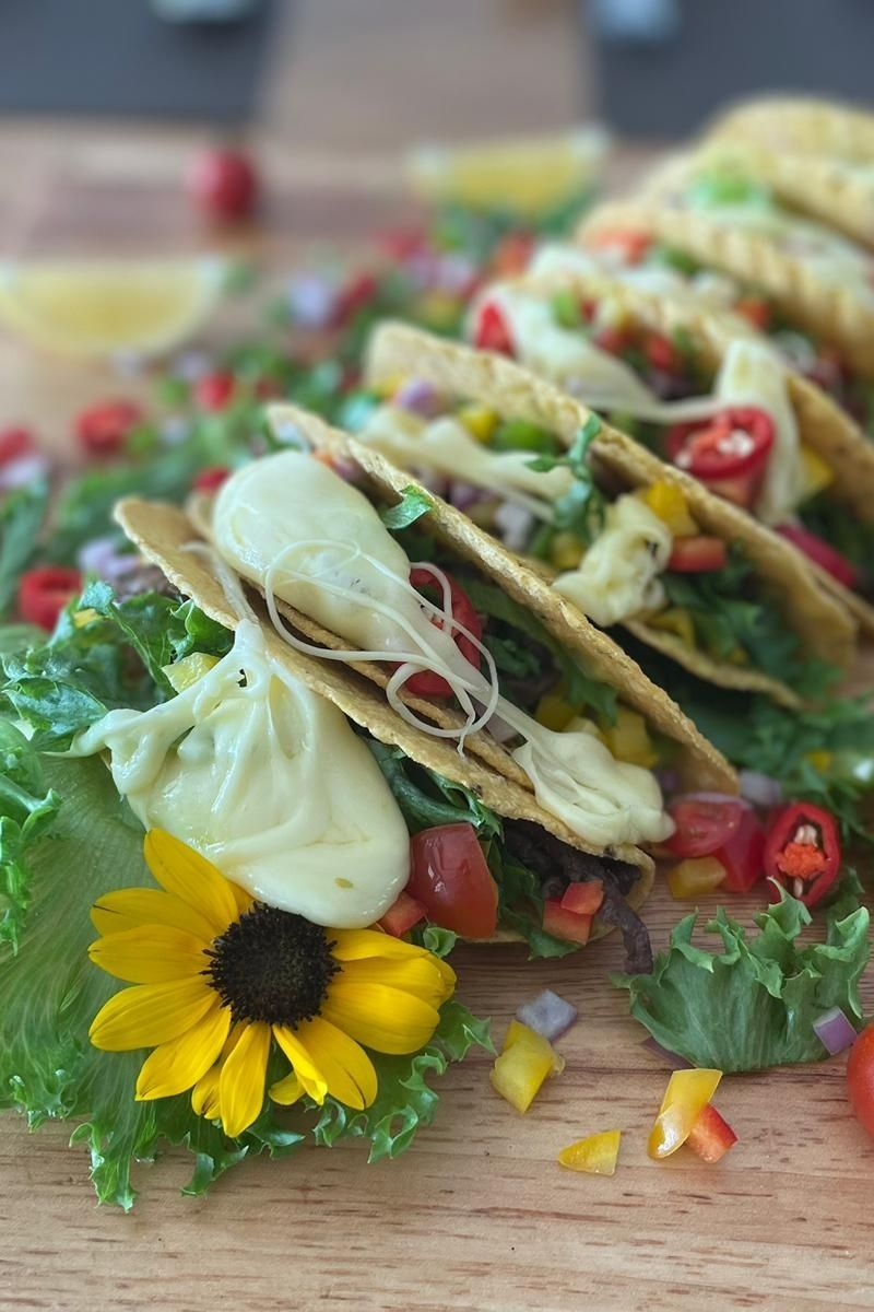 Tacos with avocado cream and vegetables on a wooden surface with a yellow flower.