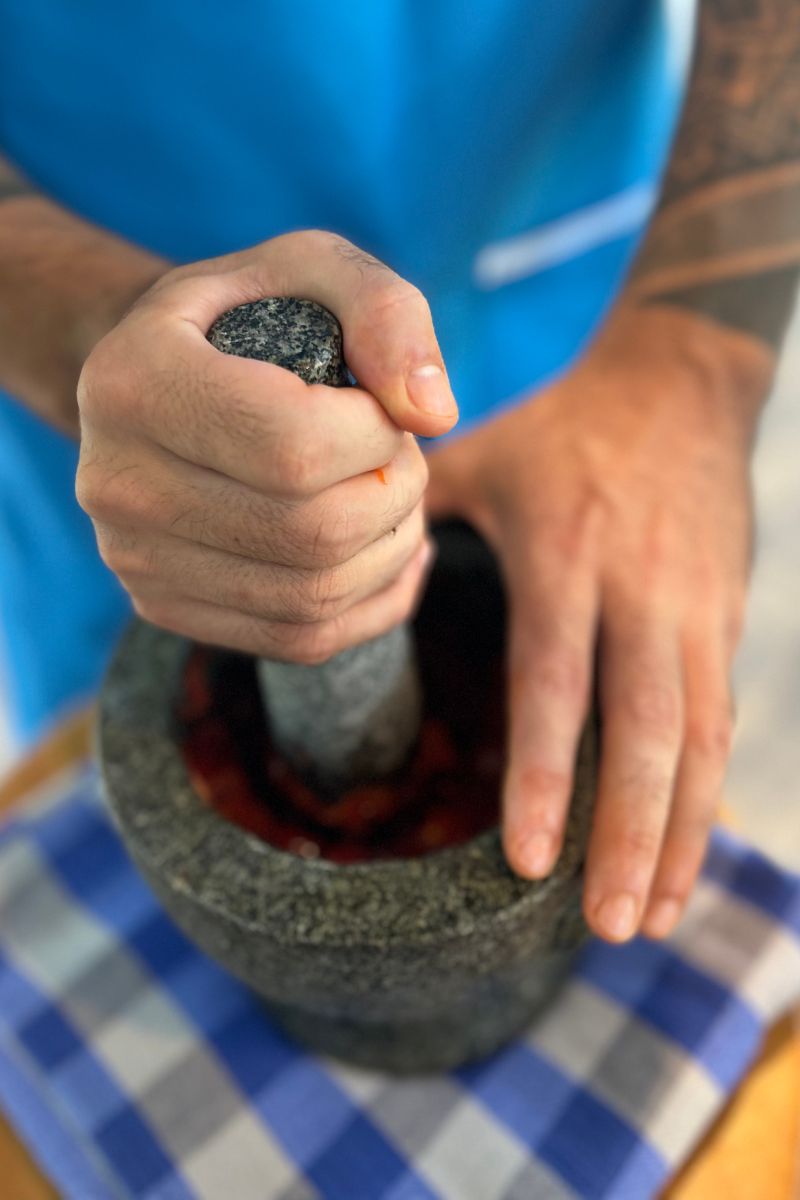 Person holding a stone pestle over a mortar on a checkered surface