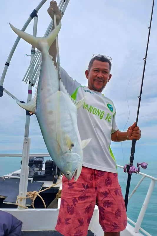 Man holding a large fish on a boat with a clear sky background