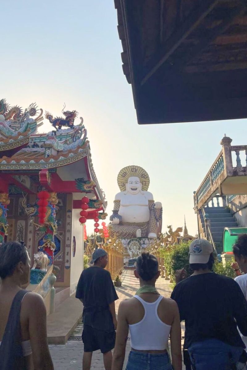 Group of people visiting a large statue in an outdoor setting with colorful architecture.