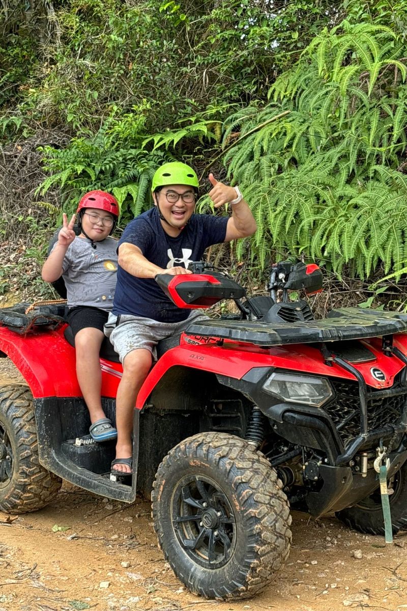 Two people on a red ATV in a forest setting
