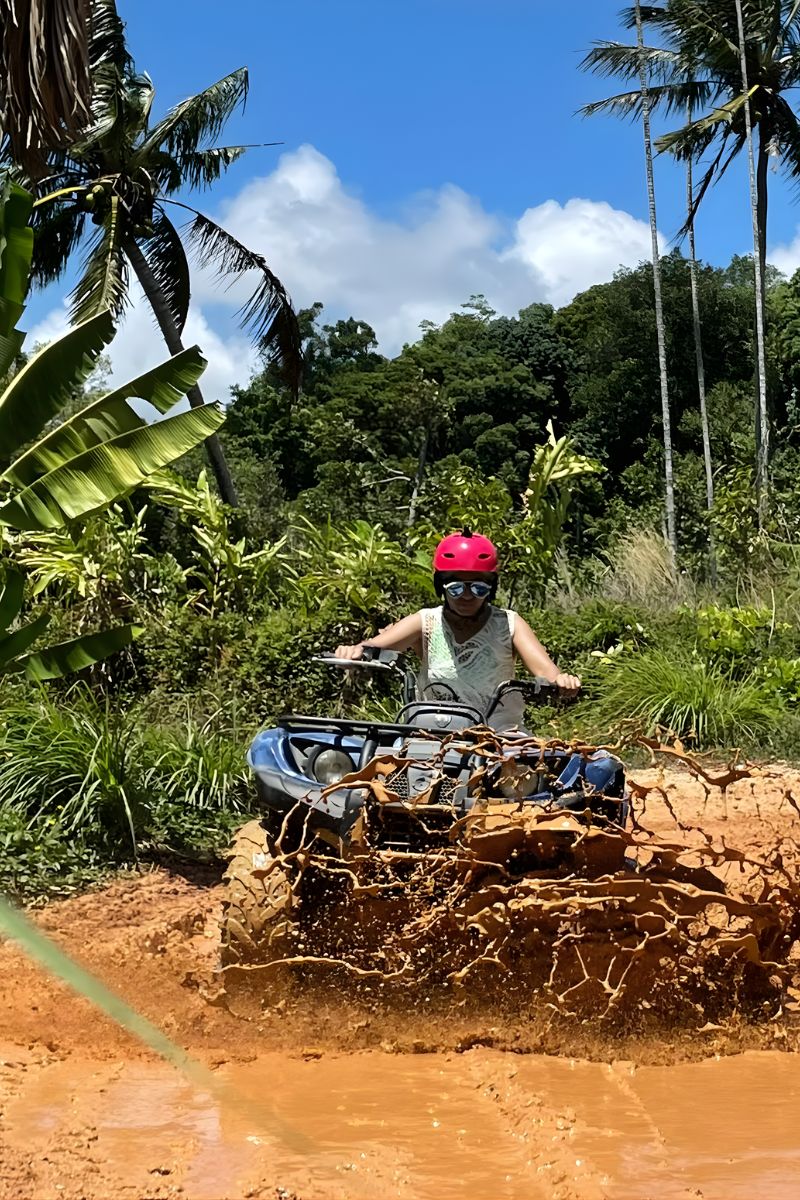 Person driving an ATV through a muddy trail in a tropical forest