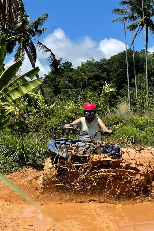 Person driving an ATV through a muddy trail in a tropical forest