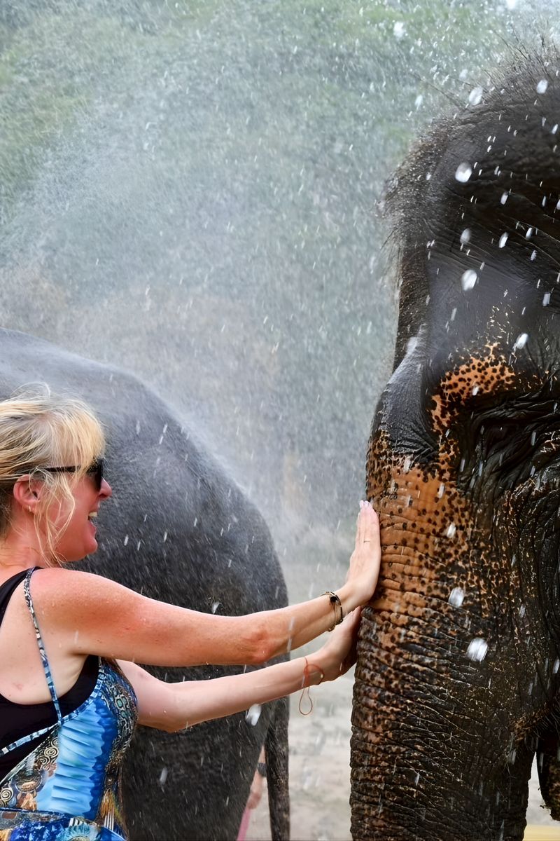 Woman washing an elephant with water, surrounded by water droplets.