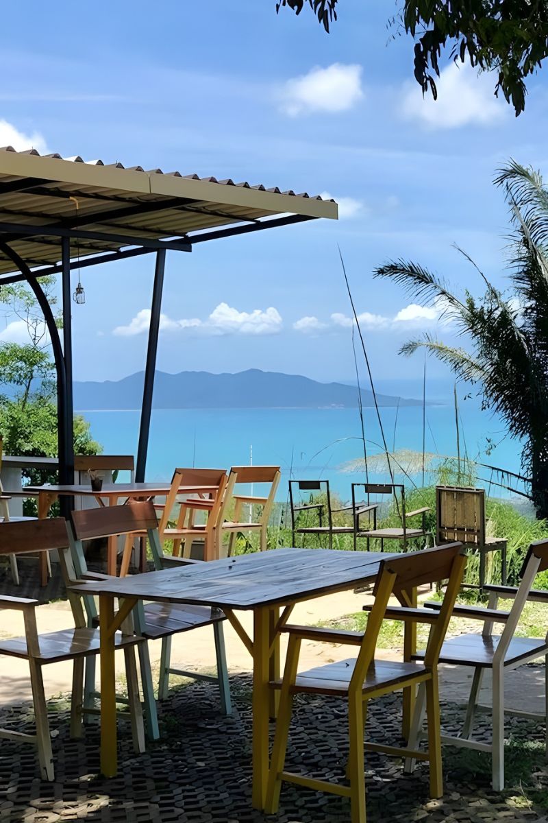 Outdoor seating area with tables and chairs overlooking a scenic view of mountains and sea.
