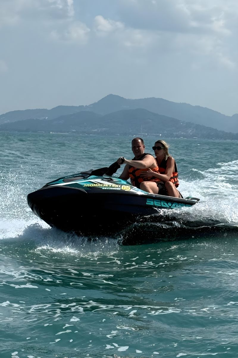 Two people riding a jet ski on choppy water with mountains in the background