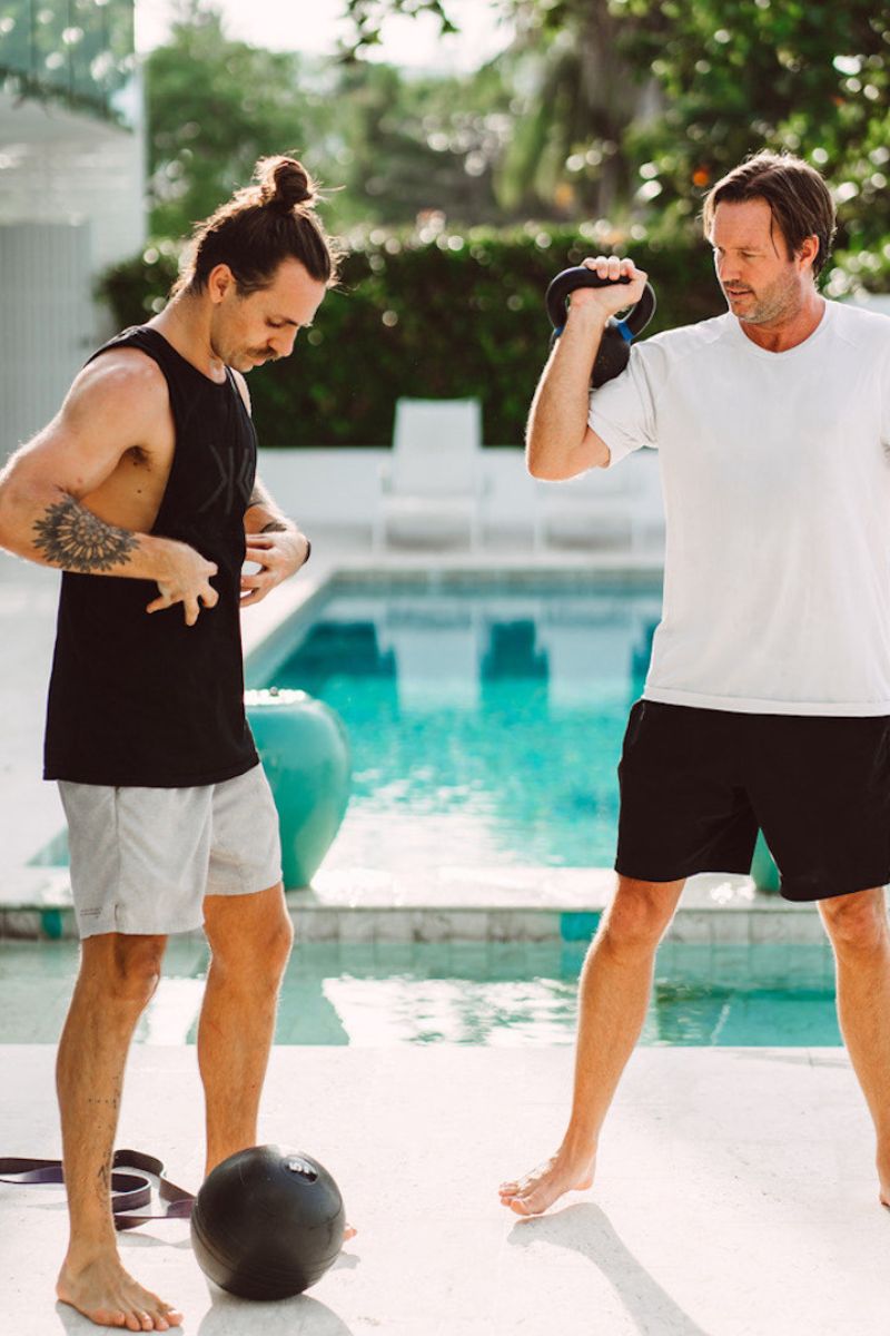Two men exercising by a poolside with a medicine ball.