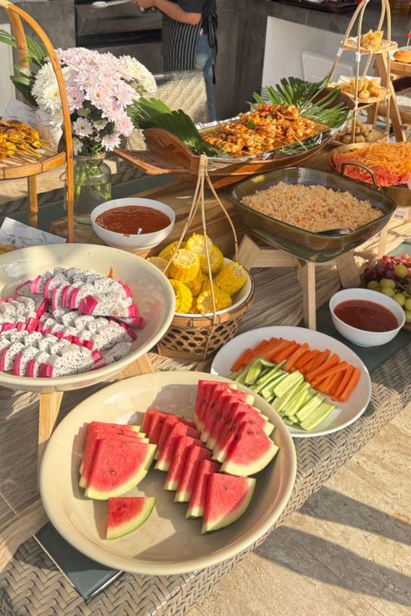 Outdoor setting with a table full of various food items including watermelon, vegetables, and bowls.