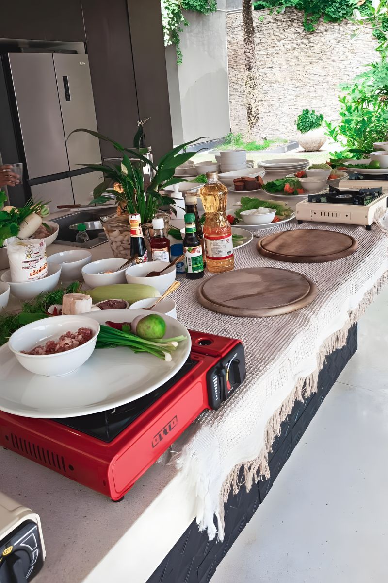 Outdoor cooking setup with a portable stove, plates, and ingredients on a table.