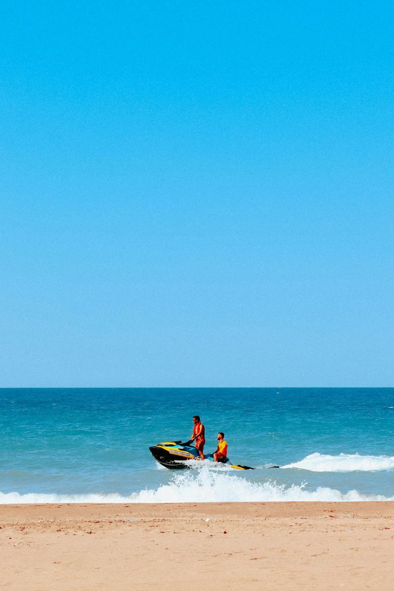 Two people on a jet ski at the beach with clear blue sky and water.