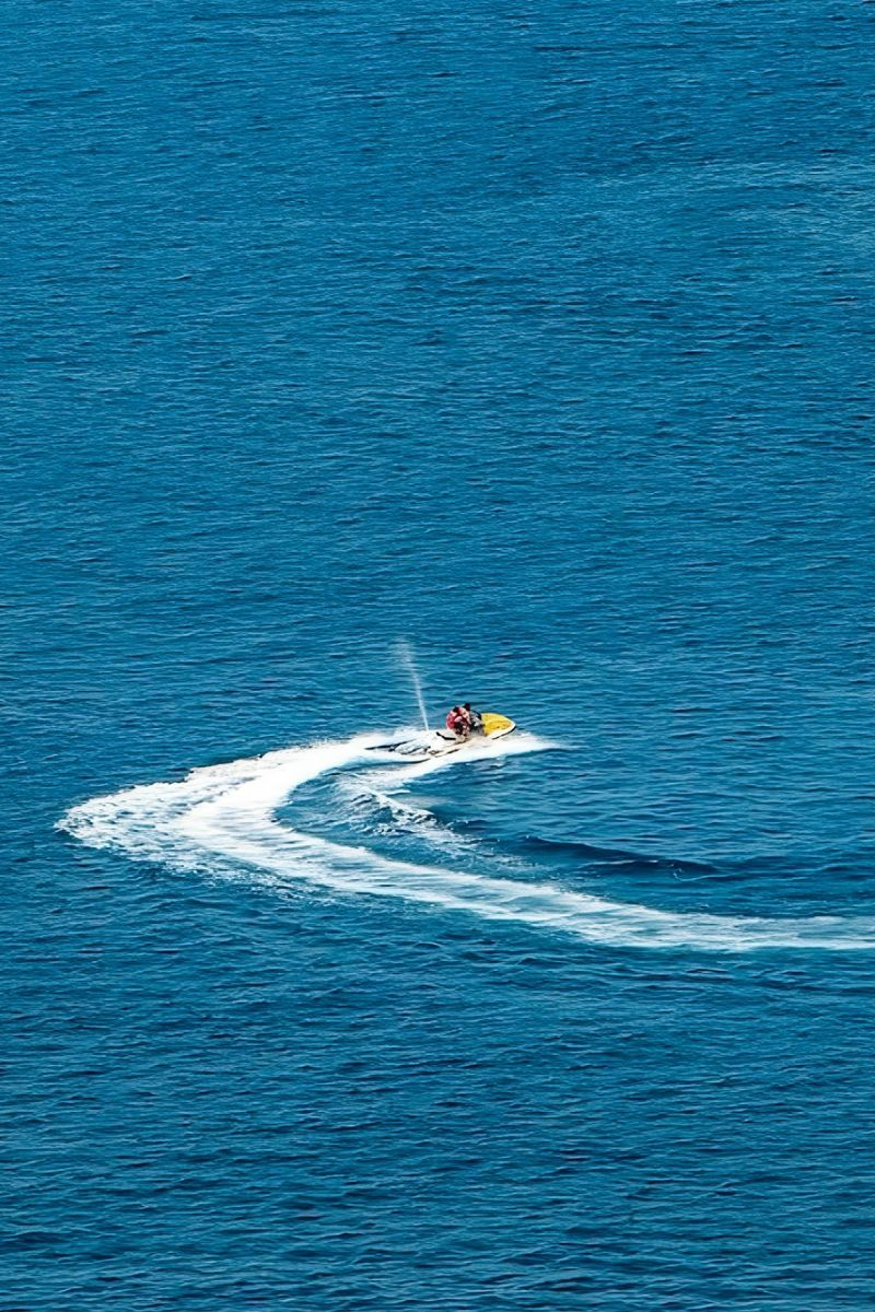 Two people on a jet ski leaving a trail of white water in the blue ocean.