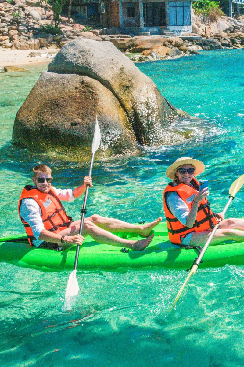 Two people in kayaks with life vests on a clear blue water background.