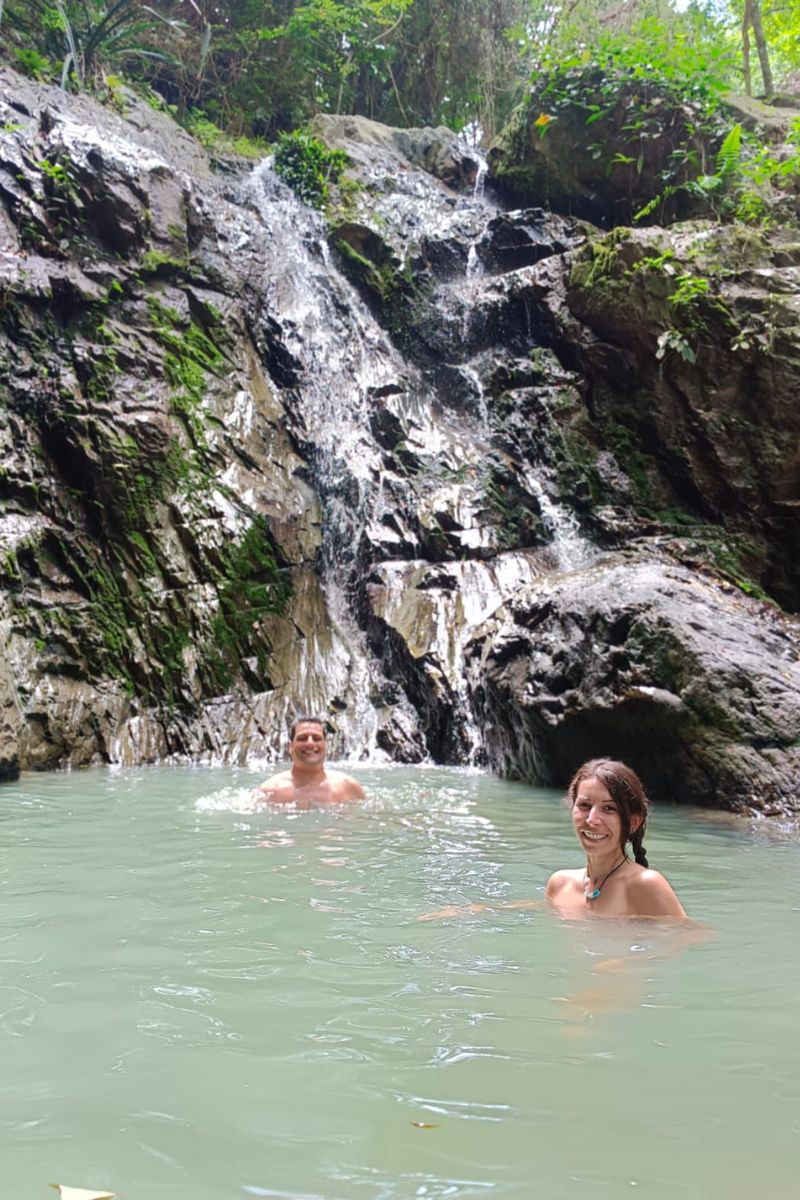 Two people in a natural pool with a waterfall in the background