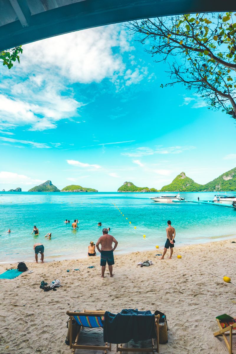 Beach scene with people enjoying the water and sand, under a clear blue sky.